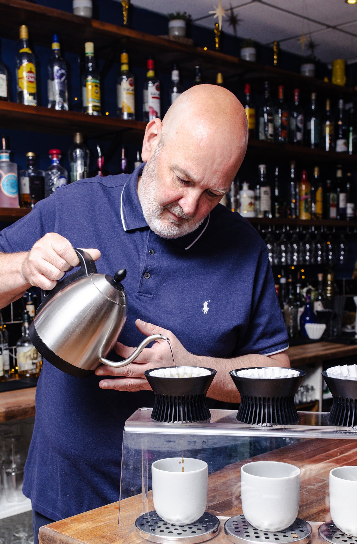 Gordon Howell preparing coffee in a bar setting with a variety of bottles in the background